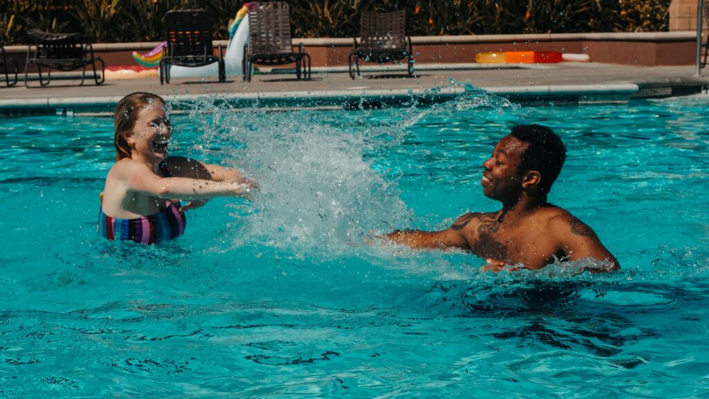 Two children playing in a pool, splashing water toward each other with smiles.