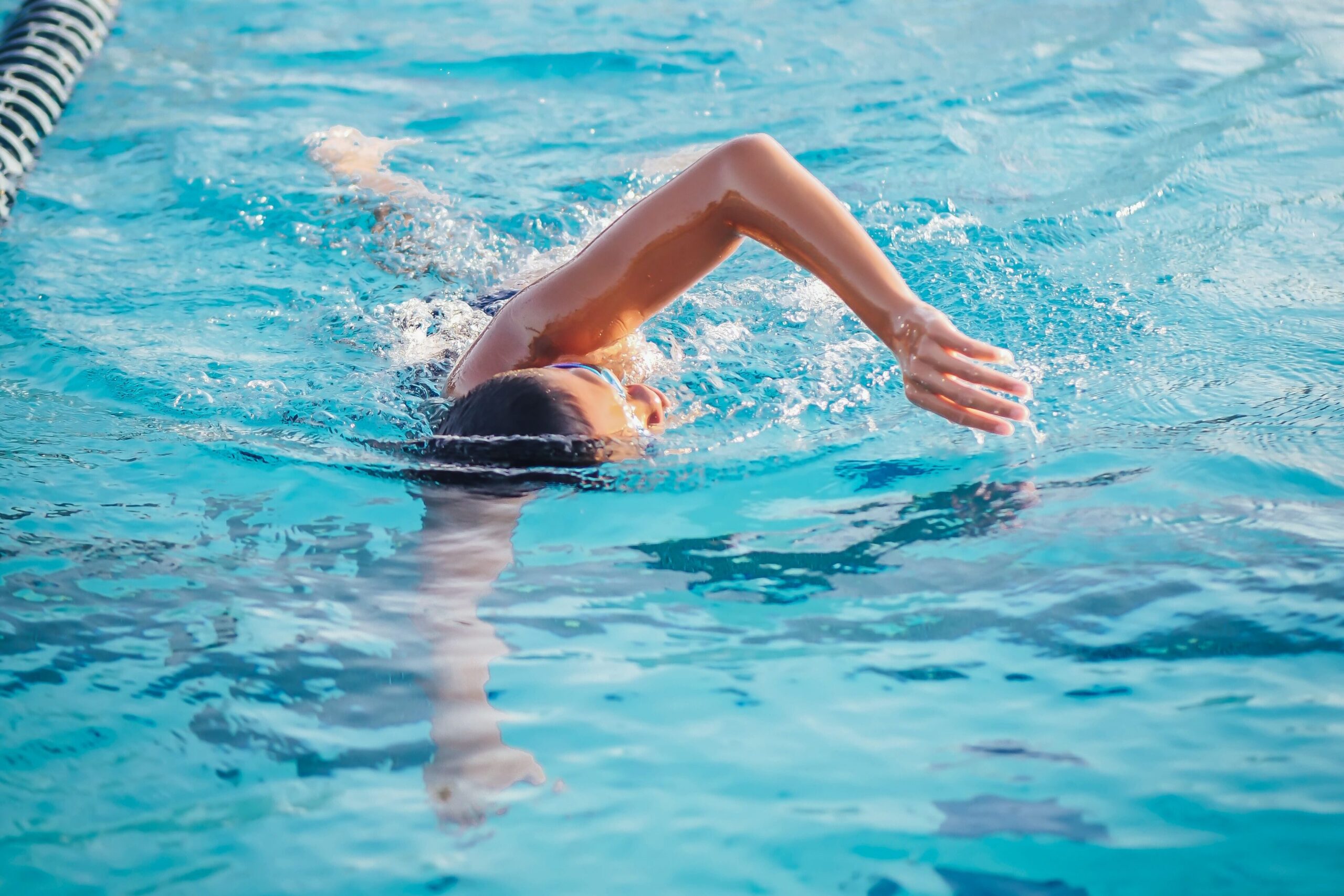 Swimmer performing freestyle stroke in a lane of a blue swimming pool, arm raised above water.